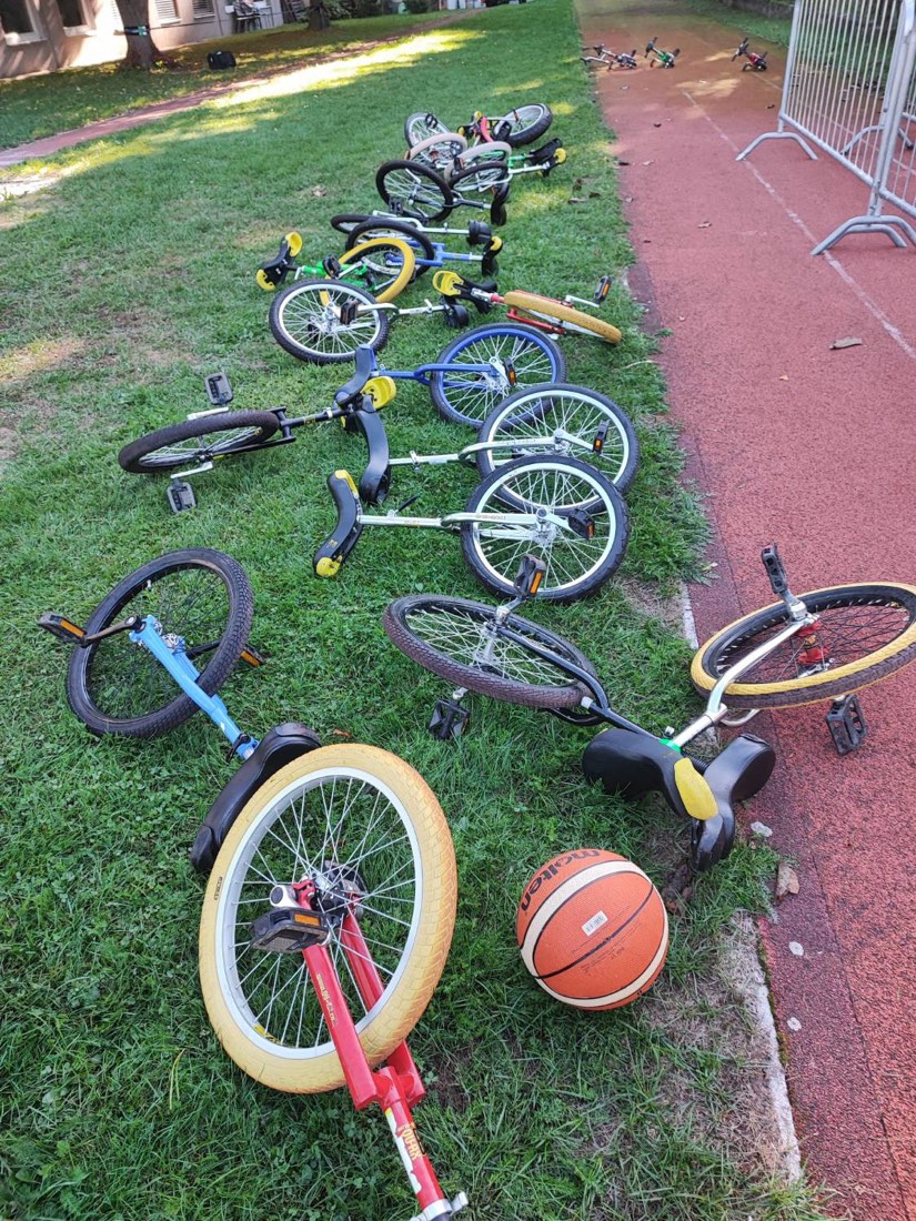 Rund ein Dutzend Einräder in verschiedenen Größen und Farben liegen aufgereiht im Gras neben der Laufbahn.