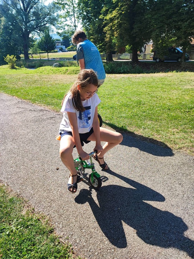 Ein Mädchen fährt konzentriert auf einem winzigen grünen Minibike über den Parkweg.