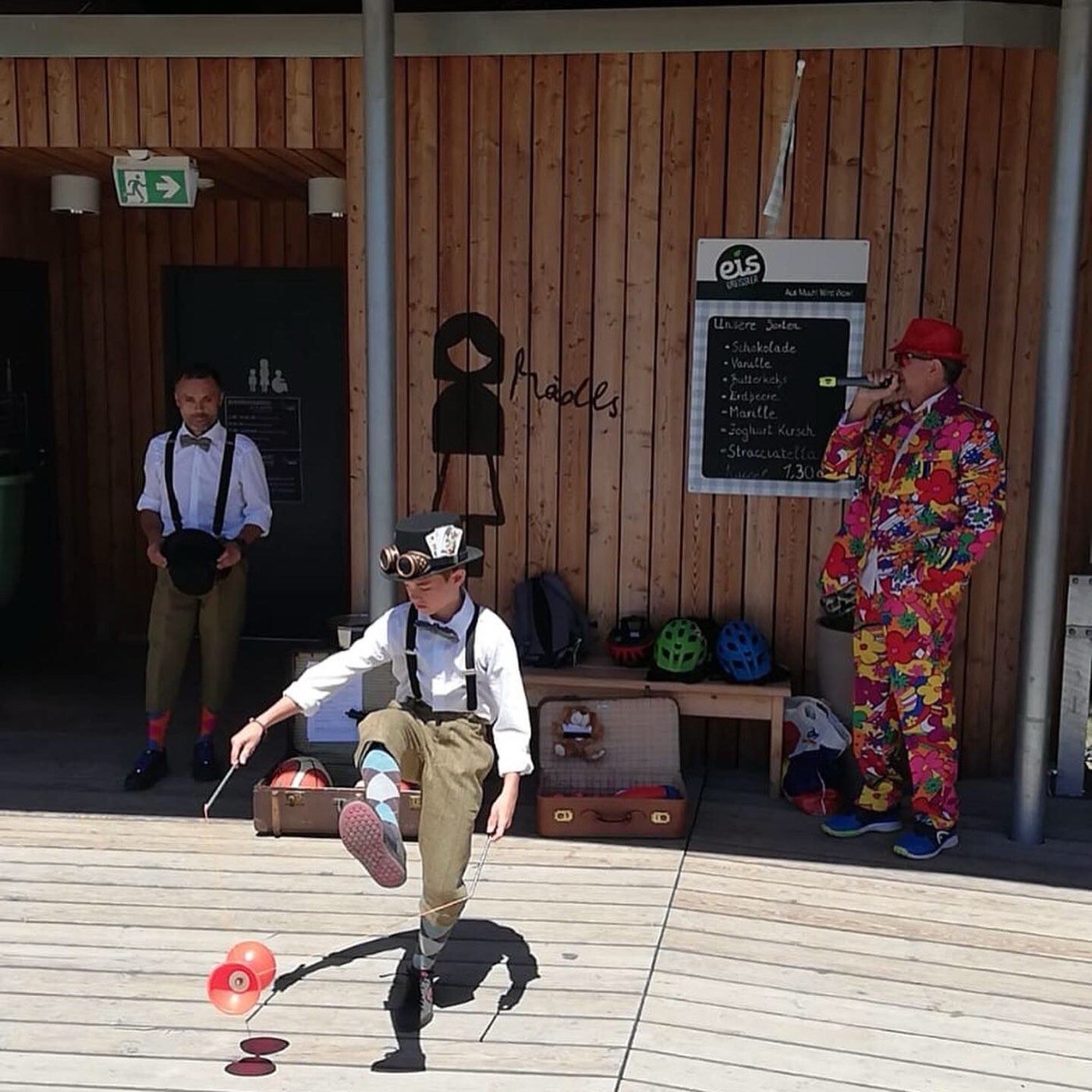Lukas spielt bei einer Show ein Diabolo unter dem Bein durch, im Hintergrund Leo und Moderator Erwin „The Voice“ Pieler im bunten Blumenanzug.